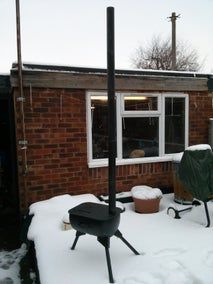 a backyard covered in snow next to a brick building with a grill on the outside