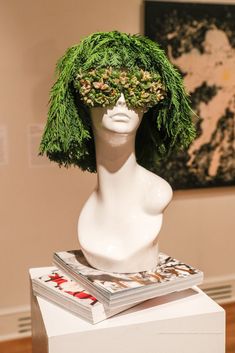 a white mannequin head covered in green grass and surrounded by books on top of it