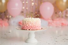 a pink and white cake with the word love on top sitting on a plate in front of balloons