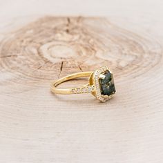 a gold ring with a green stone surrounded by white diamonds on a tree stump background