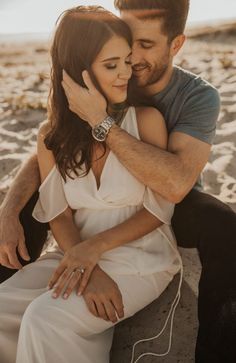 a man and woman sitting on the beach hugging each other with headphones in their ears