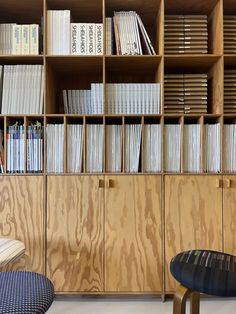 the bookshelf is filled with many books and there are two stools in front of it