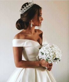 a woman in a white dress holding a bouquet of flowers and wearing a tiara