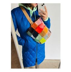 a woman taking a selfie with her cell phone wearing a blue jacket and multicolored bag