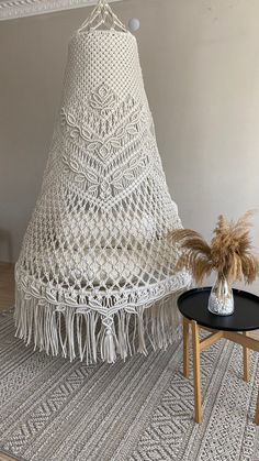 a white crocheted hammock hanging from the ceiling next to a small table