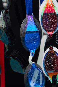 several colorful ear buds hanging from hooks with water droplets on them and one is blue, the other is red