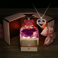 a teddy bear in a gift box with flowers and a heart pendant on the necklace