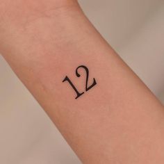 a small wrist tattoo with the number twelve on it's left arm and an arrow in the middle