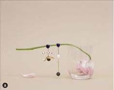 a vase with flowers and jewelry hanging from it's side on a white surface