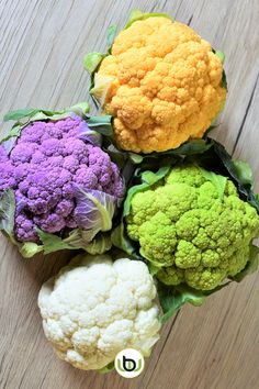 four different colored cauliflower heads on a wooden surface with the letter d below them