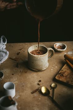 a person pouring chocolate into a cup on a table with spoons and other items