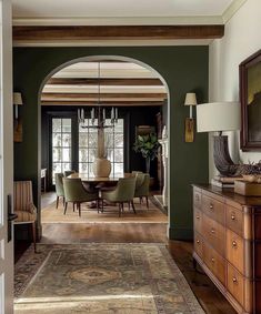 a dining room with green walls and wooden floors, an archway leading to the living room