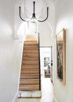 a staircase leading up to a living room with white walls and wood flooring on either side