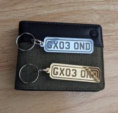 two keychains are sitting next to each other on a wooden surface, one has a metal tag that says gxo3 and the other is gold