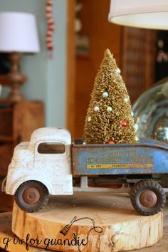 a toy truck with a christmas tree in the back is sitting on a wooden stump