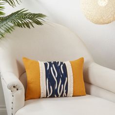 a white chair with a yellow and blue pillow on it next to a potted plant