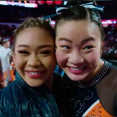 two young women standing next to each other in front of a crowd at a sporting event