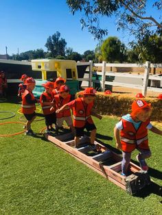 children in life vests are standing on a wooden plank with water hoses attached to it