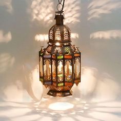 a lamp hanging from the ceiling in front of a white wall with shadows on it