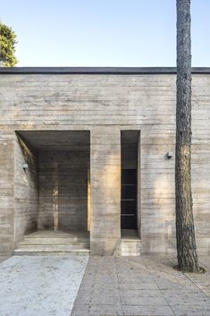 an empty concrete building with two trees in the foreground and one tree on the other side