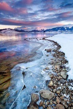 an icy lake with rocks and ice on the shore under a cloudy sky at sunset