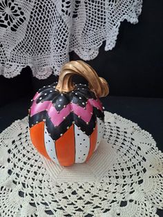 an orange and pink painted pumpkin sitting on top of a doily