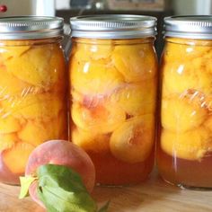 three jars filled with peaches sitting on top of a wooden table next to a plant