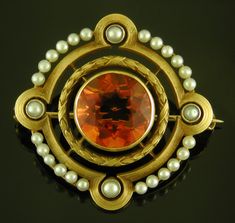 A vibrant orange citrine glows from within a ribbon-tied laurel wreath framed by luminous pearls set in a reeded gold border.  This striking brooch was created by Hans Brassler in 14kt gold circa 1910. The reverse of the brooch is as beautifully crafted as the front.  Note the sturdiness and details of the frame that protects the gemstone and pearls and assures the integrity of the jewel with the passage of time.  The design of the front is echoed on the reverse in low relief - an added touch of elegance found on some of Brassler's finer jewels.  Finally, a strong pin stem and an early safety clasp secure this brooch when worn on a lapel, collar or hat band.     Measurements:  This 14kt gold brooch is 1 1/8" by 1 1/8" and weighs 6.4 grams. Hans Brassler was an imaginative jewelry designer, Elegant Orange Brooch Jewelry, Orange Brooch Jewelry For Formal Occasions, Formal Orange Brooch Jewelry, Elegant Orange Brooches For Gifts, Orange Victorian Jewelry For Formal Occasions, Orange Citrine, Gold Brooch, Passage Of Time, Antique Brooches