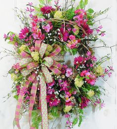 a wreath with pink and yellow flowers hanging on the front door, decorated with ribbon