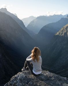 a woman sitting on top of a mountain looking at the mountains