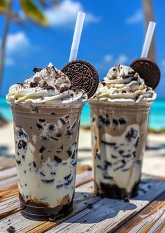 two ice cream sundaes sitting on top of a wooden table next to the ocean