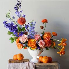 an arrangement of flowers and oranges in a white vase