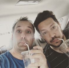 two men sitting in the back seat of a car drinking milk and straws from plastic cups