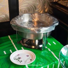 a table topped with a metal bowl and plate on top of a green cloth covered table