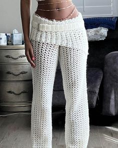 a woman standing in front of a couch wearing white knitted pants and crop top