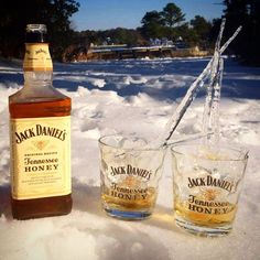 two shot glasses sitting in the snow next to a bottle of jack daniels honey