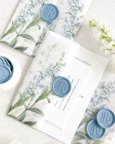 two wax seals sitting on top of a card next to some white and blue flowers