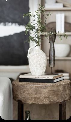 a white vase sitting on top of a wooden table next to a book and plant