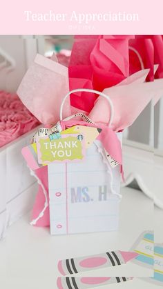 a gift bag with pink tissue paper on it and the words teacher appreciation written in white