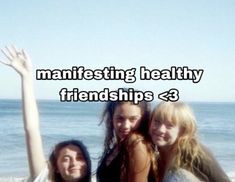 three girls are standing on the beach with their arms in the air and one girl is holding her hand up