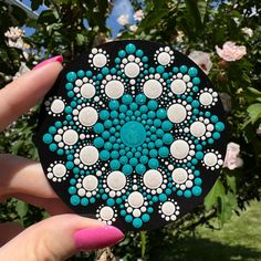 a hand holding a black and white disc with blue dots on the center, surrounded by pink flowers