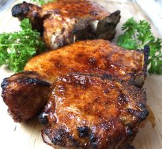 two pieces of meat sitting on top of a wooden cutting board next to parsley