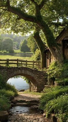 a stone bridge over a small stream in the middle of a lush green field with trees