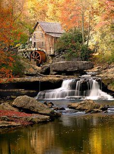 an old mill in the fall with water running down it's sides and trees surrounding it