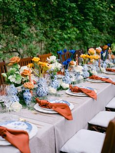 an outdoor table set with blue and white dishes, orange napkins, and flowers