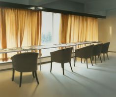 an empty conference room with long tables and chairs in front of large windows that have yellow drapes on them