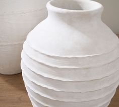 two white vases sitting next to each other on a wooden table with wood flooring