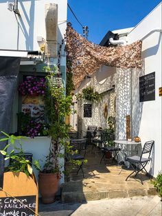 an outdoor cafe with tables and chairs on the side walk, next to potted plants