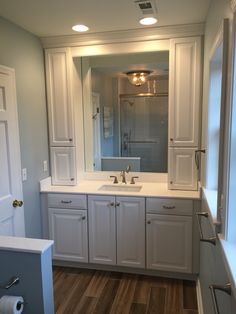 a bathroom with white cabinets and wood flooring, lights on above the sink area