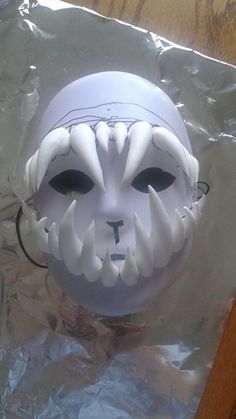 a white mask with black eyes on top of aluminum foil wrapped in plastic wrapping paper